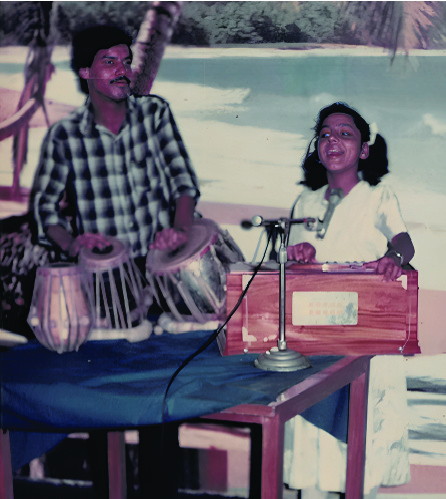 A boy playing tabla beside a girl singing at a harmonium