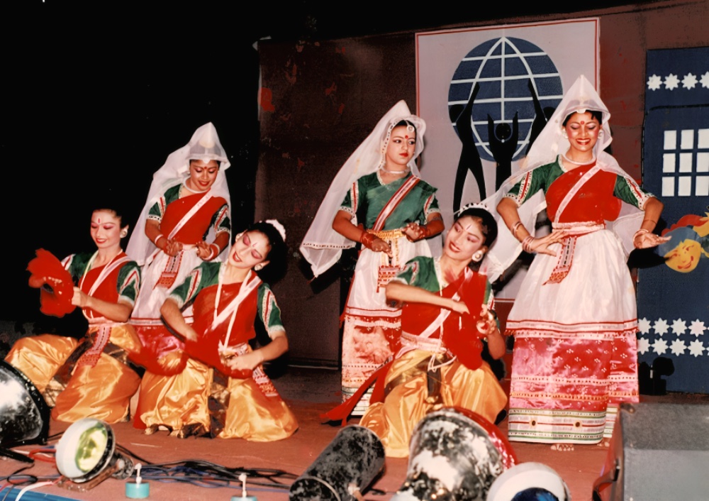 Dancers in red, green and white costume performing on a stage before the organization’s emblem