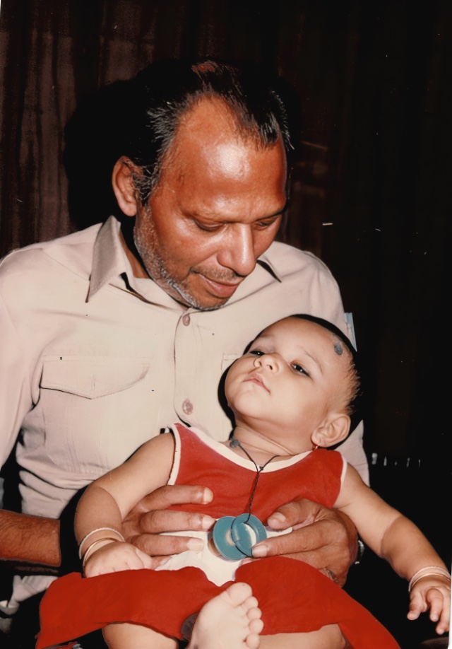 A man holding an infant in a red dress on his lap