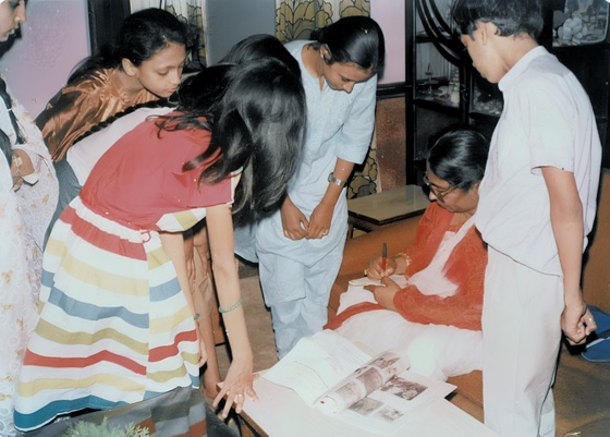 Visitors gathered around a seated woman signing papers at a table